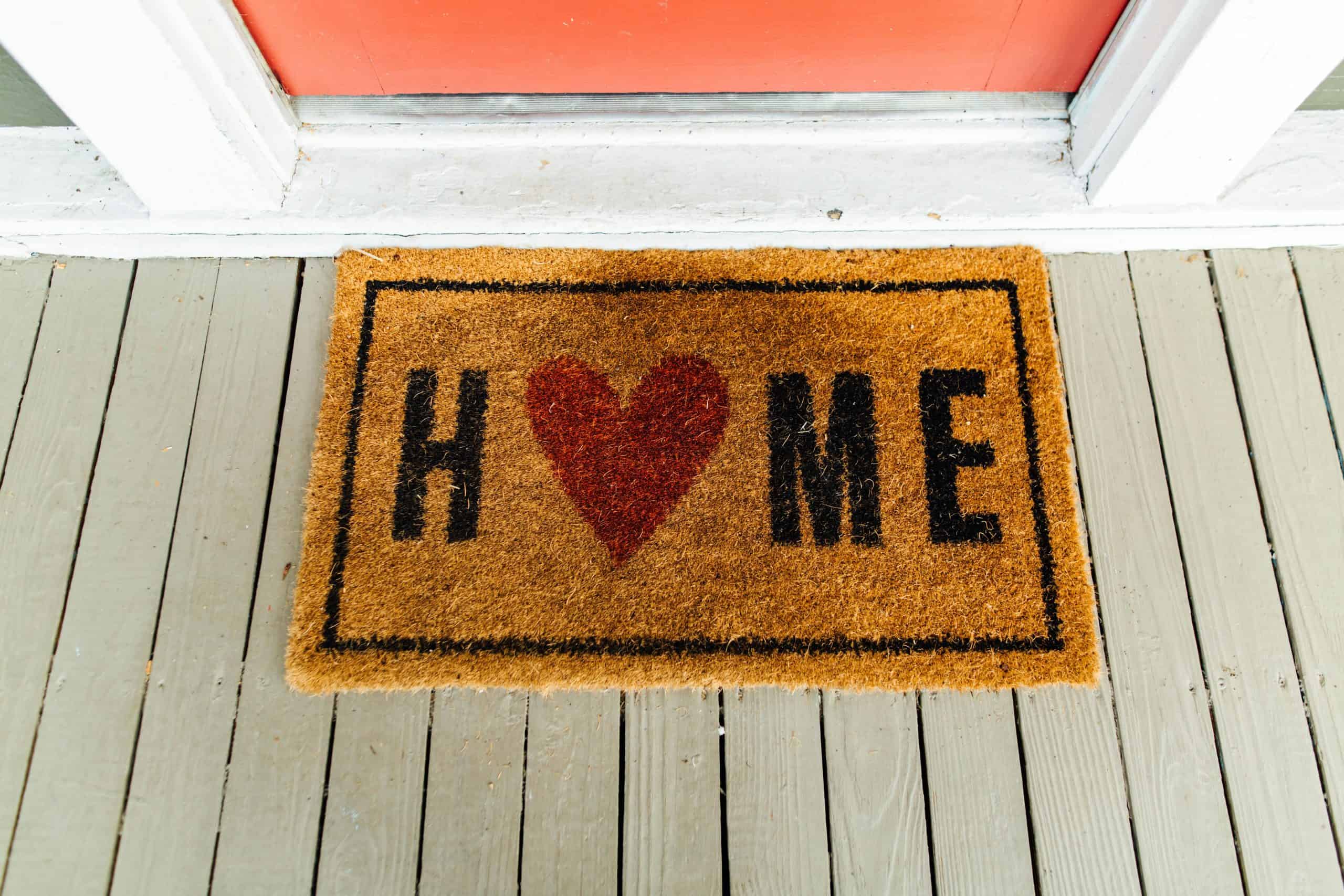 A straw welcome mat with with the word "Home" with a red heart for the "O" in home.