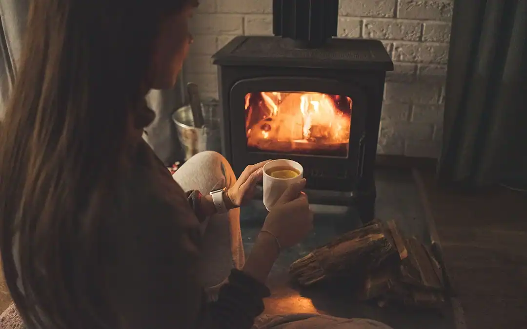 A woman sitting by a cozy fireplace with a coffee in hand