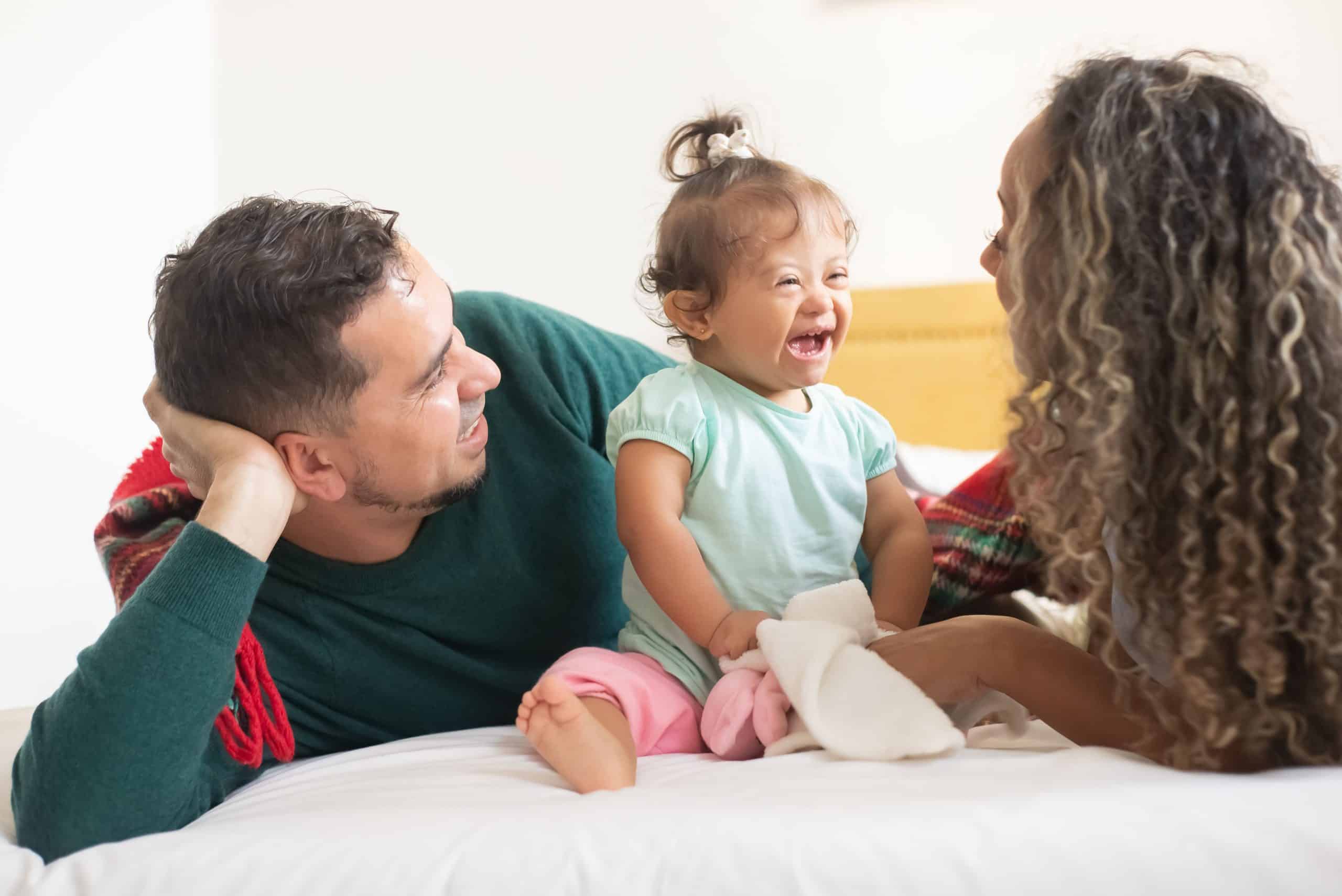 Young parents laughing and playing with their daughter who has Down syndrome.